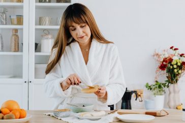 A woman in a bathrobe preparing breakfast in a home kitchen.