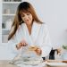 A woman in a bathrobe preparing breakfast in a home kitchen.